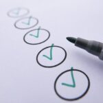 Close-up of a checklist with green checkmarks on white paper using a marker.